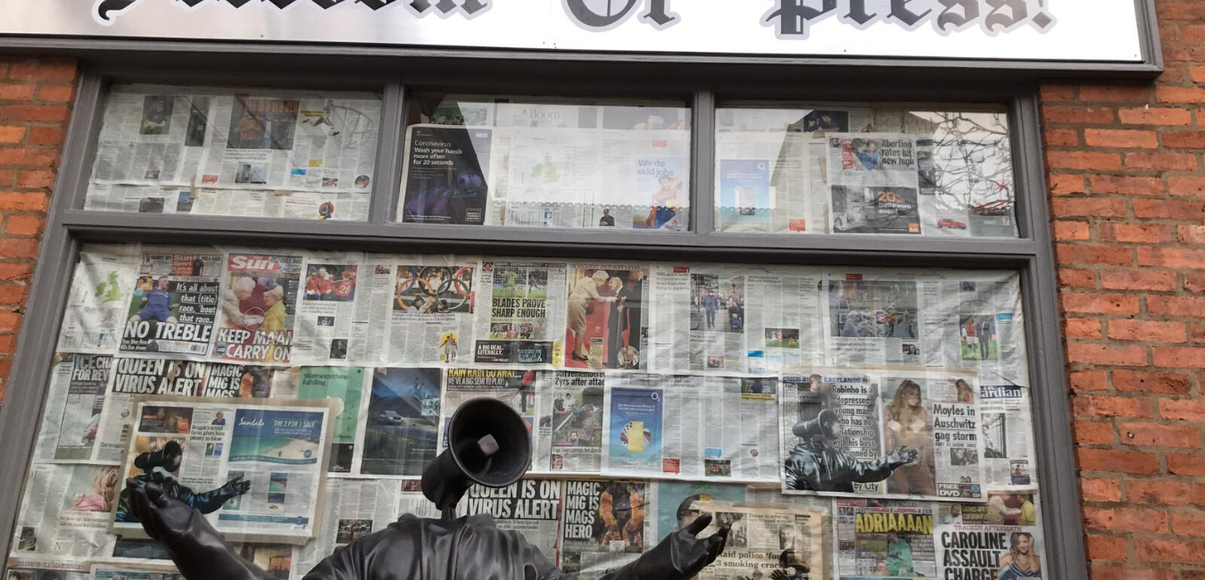 Sculpture against backdrop of newspaper and brick wall